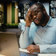 Black troubled worker rubbing his head in frustration and weariness, expressing fatigue and discomfort due to intense workload or failure. Angry frustrated man feels under pressure.